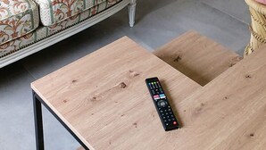 Una sala de estar moderna con una escalera de madera, un sofá estampado, un cojín oscuro, una mesa de centro de madera y un control remoto.