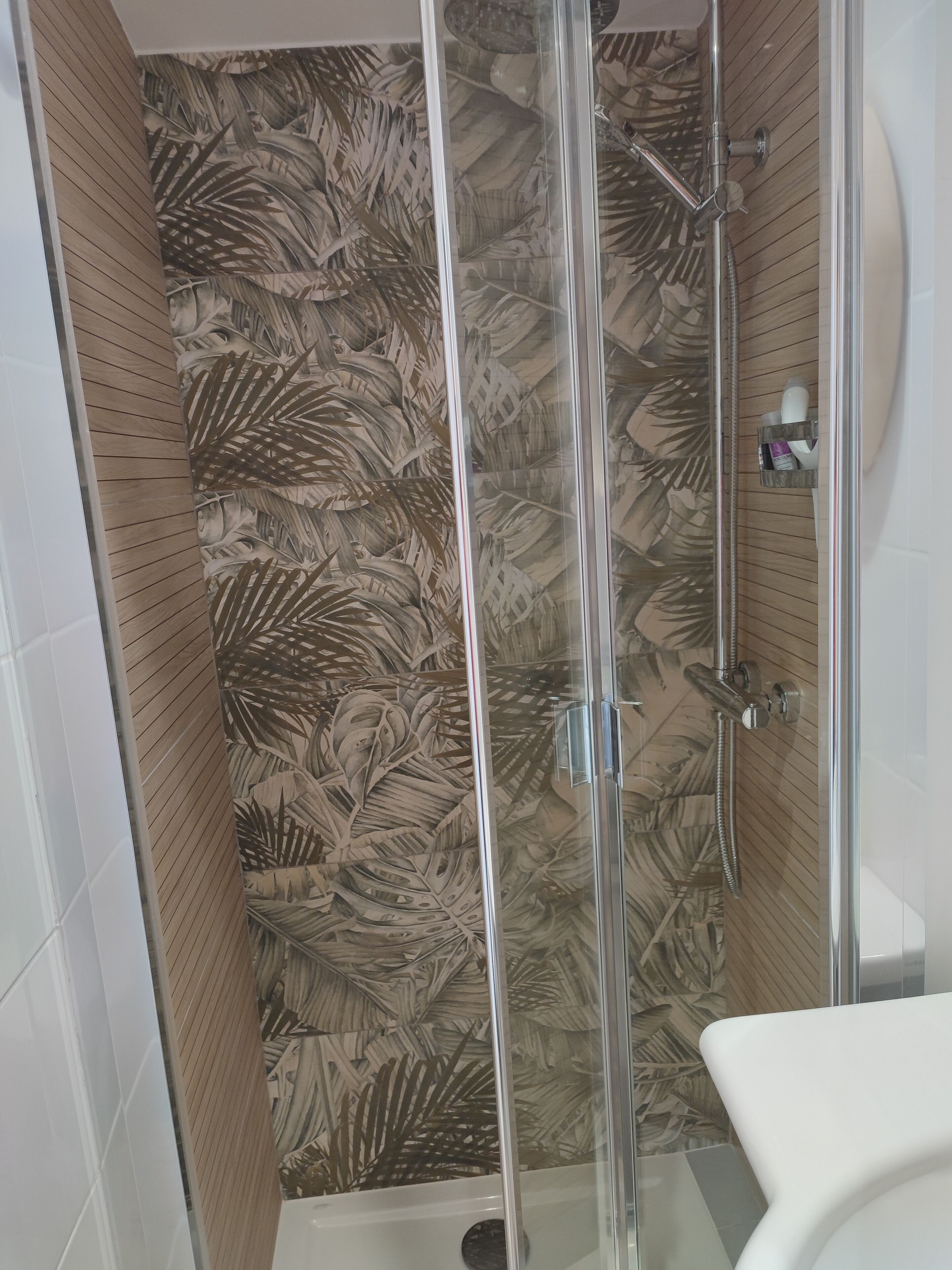 Une douche dotée d’une porte en verre et d’un mur en panneaux de bois orné d’un motif de feuilles.