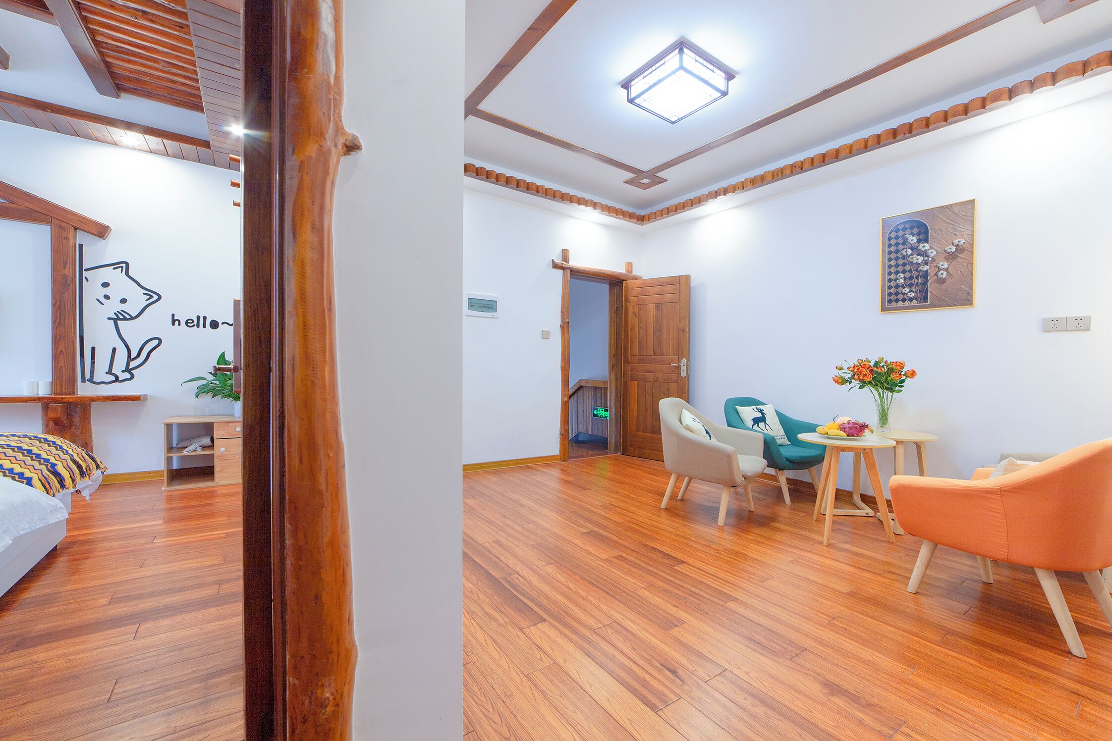 A modern room with a wooden floor, a bed with a colorful blanket, a desk, a chair, and a small table with flowers.