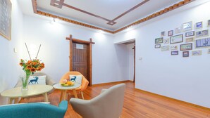 Ein Zimmer mit Holzboden, einem runden Tisch mit Blumen in einer Vase, zwei Stühlen und einer Wand, die mit gerahmten Bildern geschmückt ist.