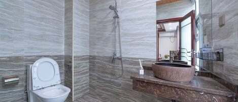 A modern bathroom with a marble floor, a toilet, a shower with a handheld showerhead, and a large sink with a marble countertop.