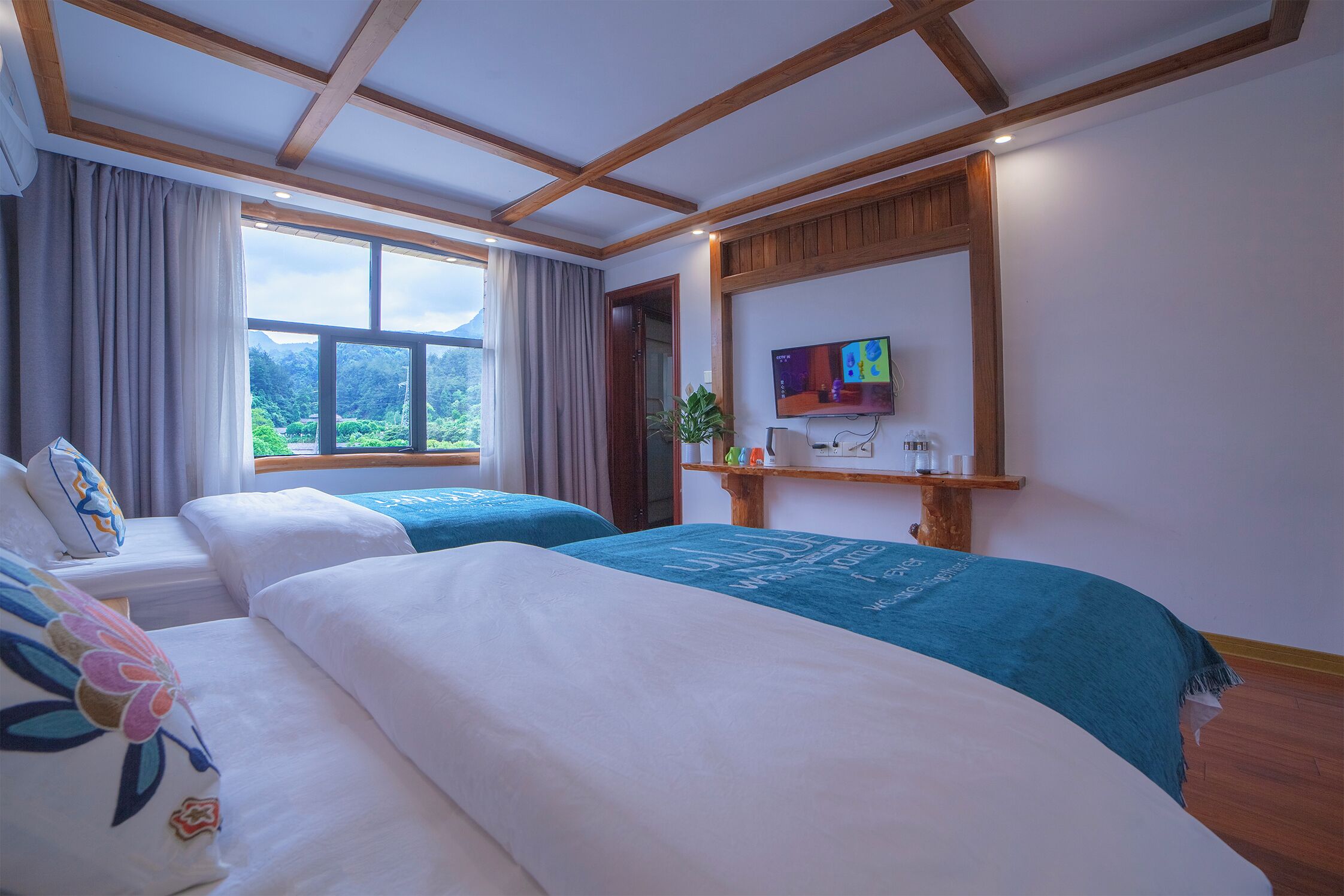 Ein Hotelzimmer mit zwei Betten, einem Fernseher, einem Fenster mit Blick auf die Berge und einer Holzbalkendecke.