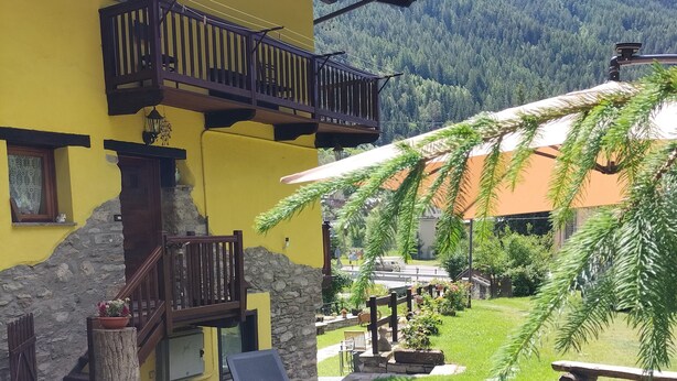 A yellow building with a balcony, stone steps, a wooden table with chairs, and a grassy garden with a mountain backdrop. - Maison du Soleil - a stone's throw from the sky, for those who love skiing and more (Maen)