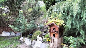 A wooden birdhouse with a sloped roof and a small entrance, surrounded by dense greenery and a wooden stump. - Maison du Soleil - a stone's throw from the sky, for those who love skiing and more (Maen)