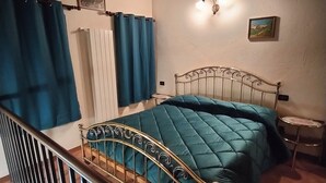 A bedroom with a metal bed frame, a blue bedspread, a nightstand, a wall-mounted light, and a painting. - Maison du Soleil - a stone's throw from the sky, for those who love skiing and more (Maen)