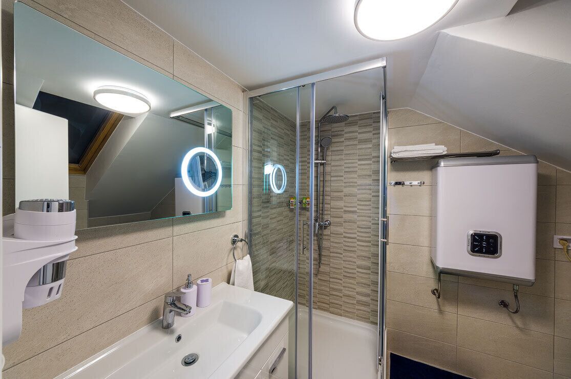 A modern bathroom with a glass-enclosed shower, a large mirror with illuminated rings, a white sink, and a built-in heater.