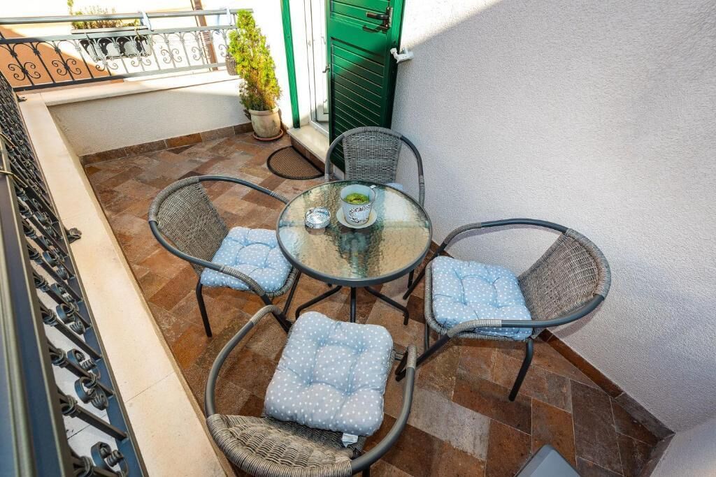 A small outdoor patio with a round glass table and four wicker chairs with blue cushions.
