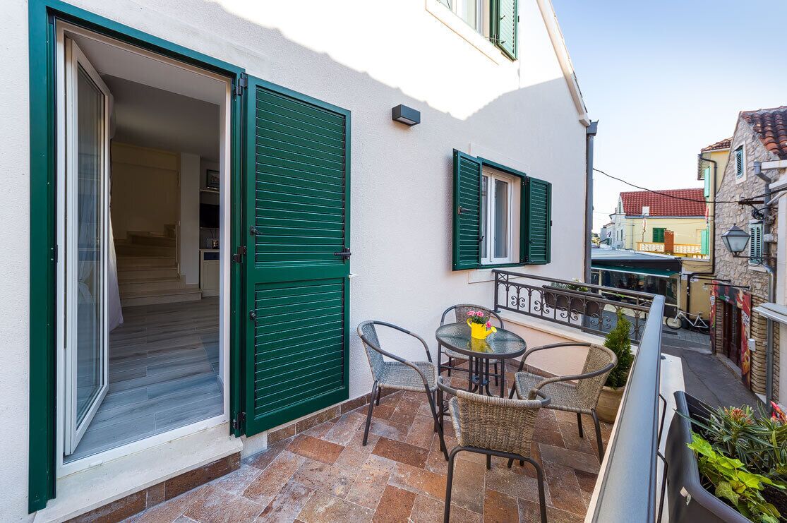 A small outdoor patio with a table and chairs, a green door, and a view of neighboring buildings.