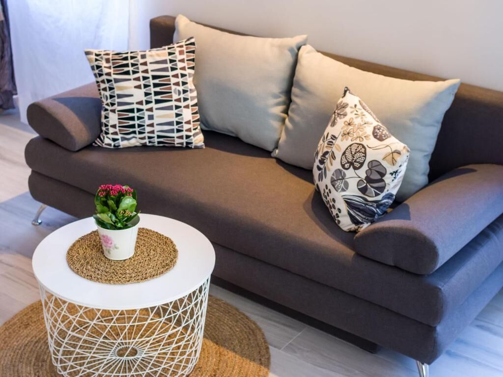 A modern living room with a dark brown sofa, patterned cushions, a white side table with a plant, and a geometric white side table.