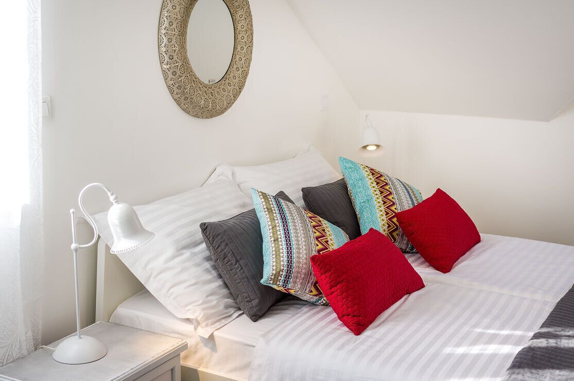 A neatly made bed with striped bedding, a white bedside lamp, and a variety of pillows.