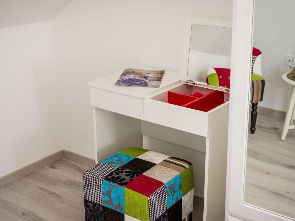 Ein weißer Waschtisch mit Spiegel, eine rote Aufbewahrungsbox und ein farbenfroher Patchwork-Hocker.