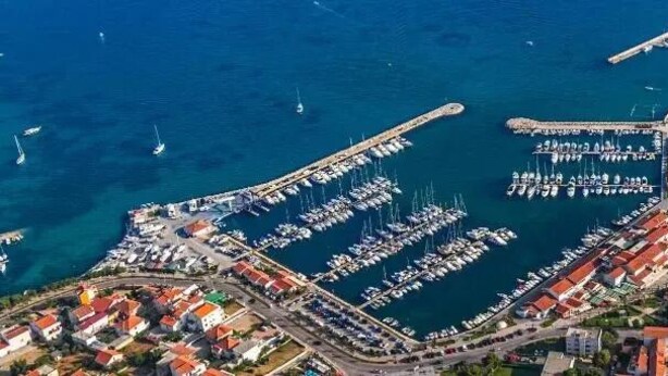 An aerial view of a coastal town with a marina, residential buildings, and a curved harbor.