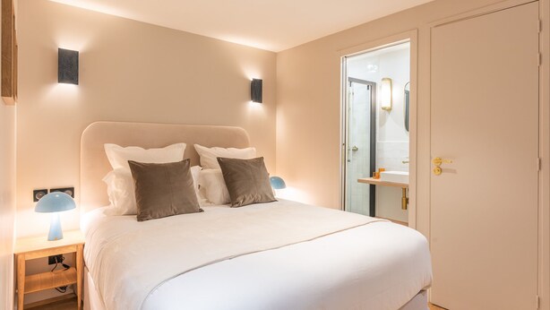 A modern bedroom with a large bed, bedside lamps, and a door leading to a bathroom. - Maison Letellier - Studio just near Eiffel Tower (Paris)
