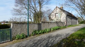 A rural road with a stone wall and a small stone building with a sloped roof. - Le Fournil (La puisaye)