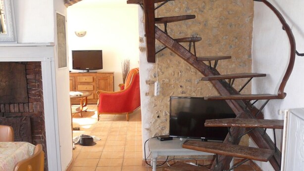 A rustic interior with a spiral staircase, a fireplace, a television, and a dining area. - Le Fournil (La puisaye)