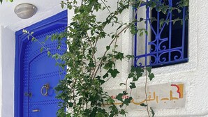 A white building with a blue door, a window with blue bars, and a potted plant in front. - Bab El Fen  (Tangier)