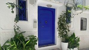 A white building with a blue door, potted plants, and a tiled pavement. - Bab El Fen  (Tangier)