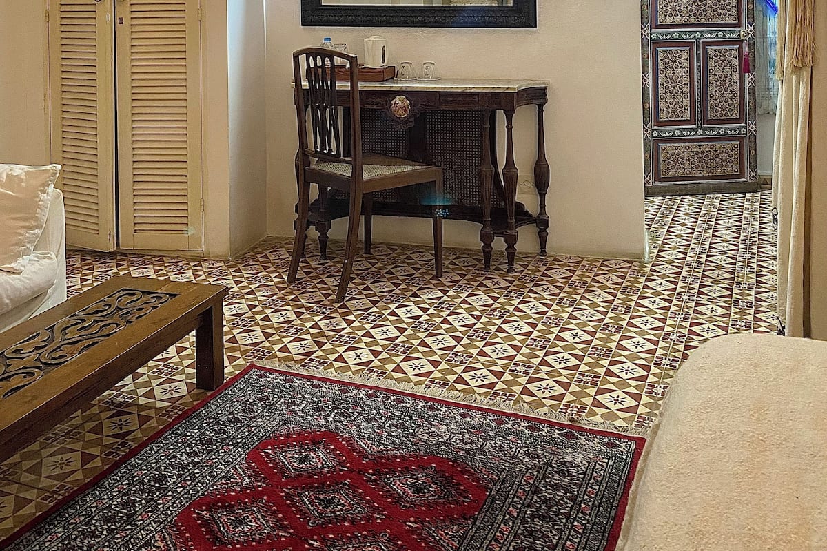 A room with a patterned floor, a wooden chair, a table, a mirror, and a hanging light fixture.