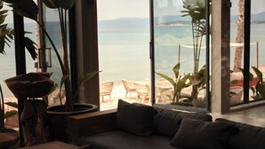 A modern living room with a large window overlooking a beach. - @Before Sunset (Cesme)