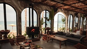 A cozy lounge area with a fireplace, comfortable seating, and a view of the beach. - @Before Sunset (Cesme)