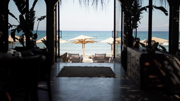 A beachside view through an arched doorway with beach umbrellas and chairs. - @Before Sunset (Cesme)