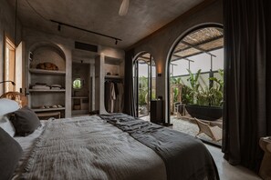 A bedroom with a large bed, a closet with shelves, a circular window, and a view of greenery outside.
