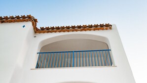 Ein weißes Gebäude mit zwei Balkonen, jeweils mit blauen Geländern, und einem braunen Ziegeldach.