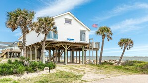 A beachfront house with a wooden deck, palm trees, and an American flag. - On Water's Edge - Literally, Direct Gulf Waterfront! (Freeport)