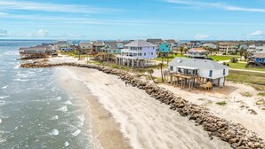 A coastal residential area with houses on stilts, a sandy beach, and a rocky shoreline. - On Water's Edge - Literally, Direct Gulf Waterfront! (Freeport)