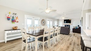 A spacious living room with a dark wooden dining table and white chairs, a gray sofa, and a TV mounted on the wall. - On Water's Edge - Literally, Direct Gulf Waterfront! (Freeport)