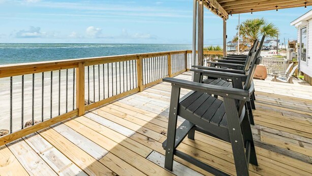 A wooden deck with a railing overlooking the ocean, a covered seating area, and a building with a beach view. - On Water's Edge - Literally, Direct Gulf Waterfront! (Freeport)