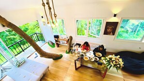 A spacious living area with a high ceiling, a hanging rope swing, a dining table with plates and cups, and a sofa.