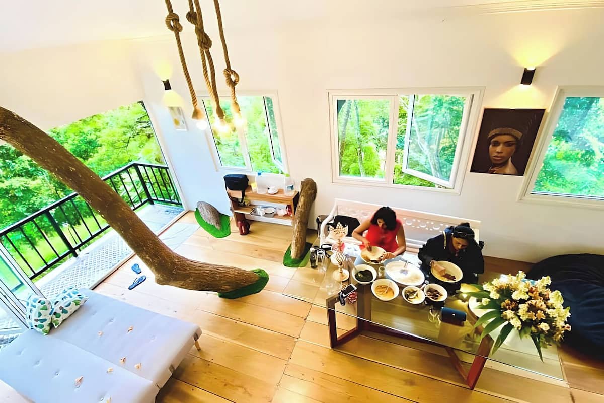 A spacious living area with a high ceiling, a hanging rope swing, a dining table with plates and cups, and a sofa.
