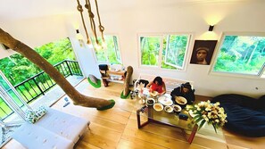 A spacious living area with a high ceiling, a hanging rope swing, a dining table with plates and cups, and a sofa.