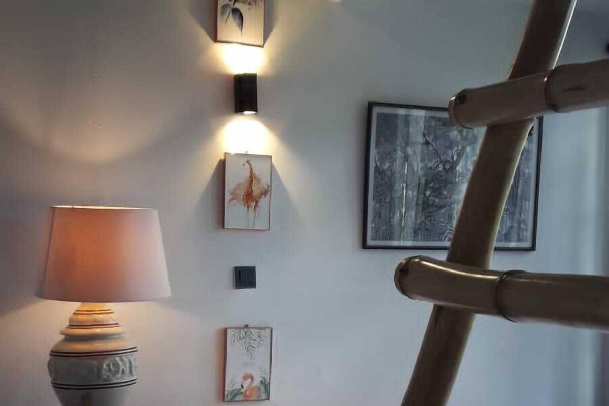 A bedroom with a bed, a bedside table with a lamp, a wooden ladder, and wall-mounted artwork.