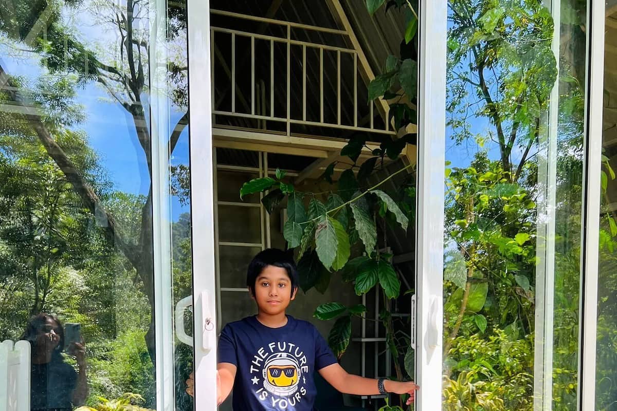 A person standing at a glass door with a view of greenery outside.