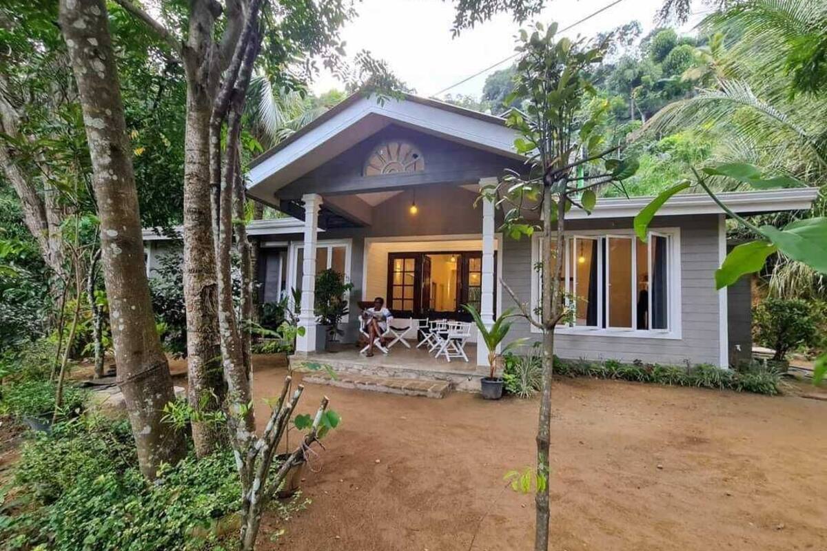 A house with a porch, surrounded by trees and a dirt driveway.