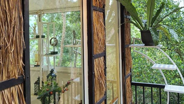 A conservatory with a glass door, straw decorations, a potted plant, and a small table.