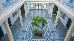 A spacious atrium with a geometric tiled floor, a central planter with a tree, and a view of the building's exterior through large windows. - The Arham Resort (Udaipur)