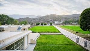 A modern building with a flat roof, a central courtyard with green grass, and a paved walkway. - The Arham Resort (Udaipur)