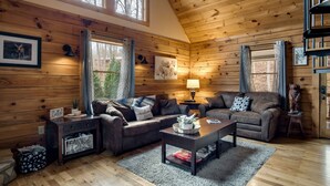 Ein Blockhaus-Interieur mit zwei Sofas, einem Couchtisch, einer Lampe und einem Fenster mit Vorhängen.