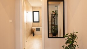 Un couloir avec un plancher en bois, une plante en pot et un miroir accroché au mur.