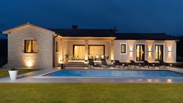 Une maison moderne dotée d’une piscine, d’une façade en pierre et d’un espace extérieur aménagé pour se détendre.