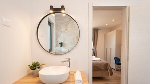 Une salle de bain moderne avec un miroir rond, un lavabo blanc et un meuble-lavabo en bois.