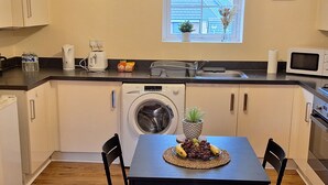 A compact kitchen with a washing machine, a microwave, and a dining area with a table and chairs. - House, Sleeps 3 With Balcony and Parking (Smethwick)