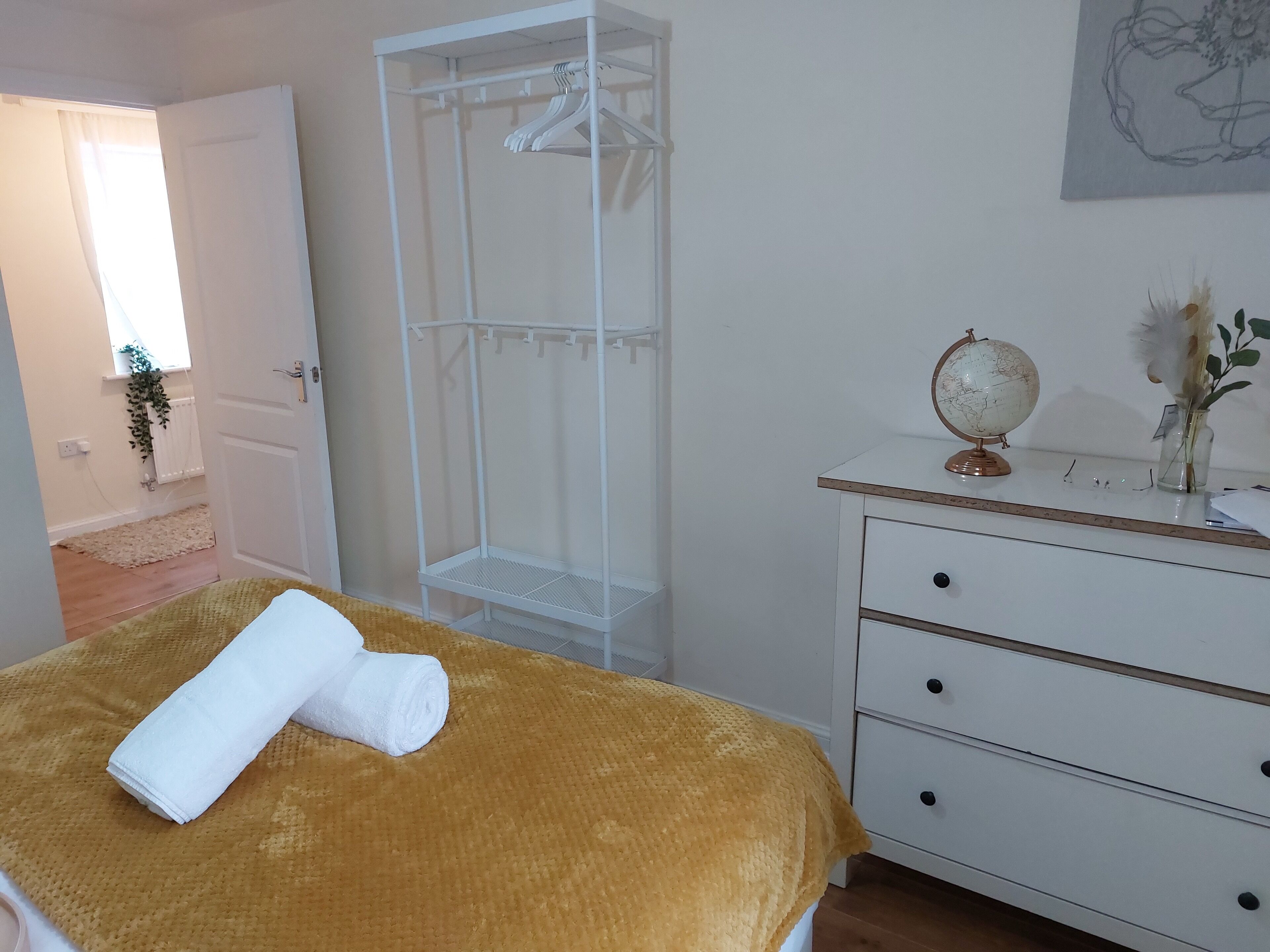 A bedroom with a bed, a white wardrobe, a dresser, a globe, and a vase with flowers.
