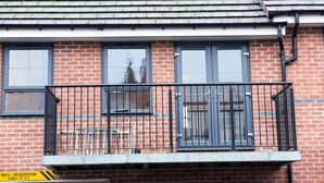 A two-story brick building with a balcony featuring a metal railing and a door. - House, Sleeps 3 With Balcony and Parking (Smethwick)