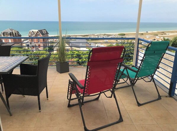 Una terraza con dos sillas y una mesa, con vista a una playa y casas.