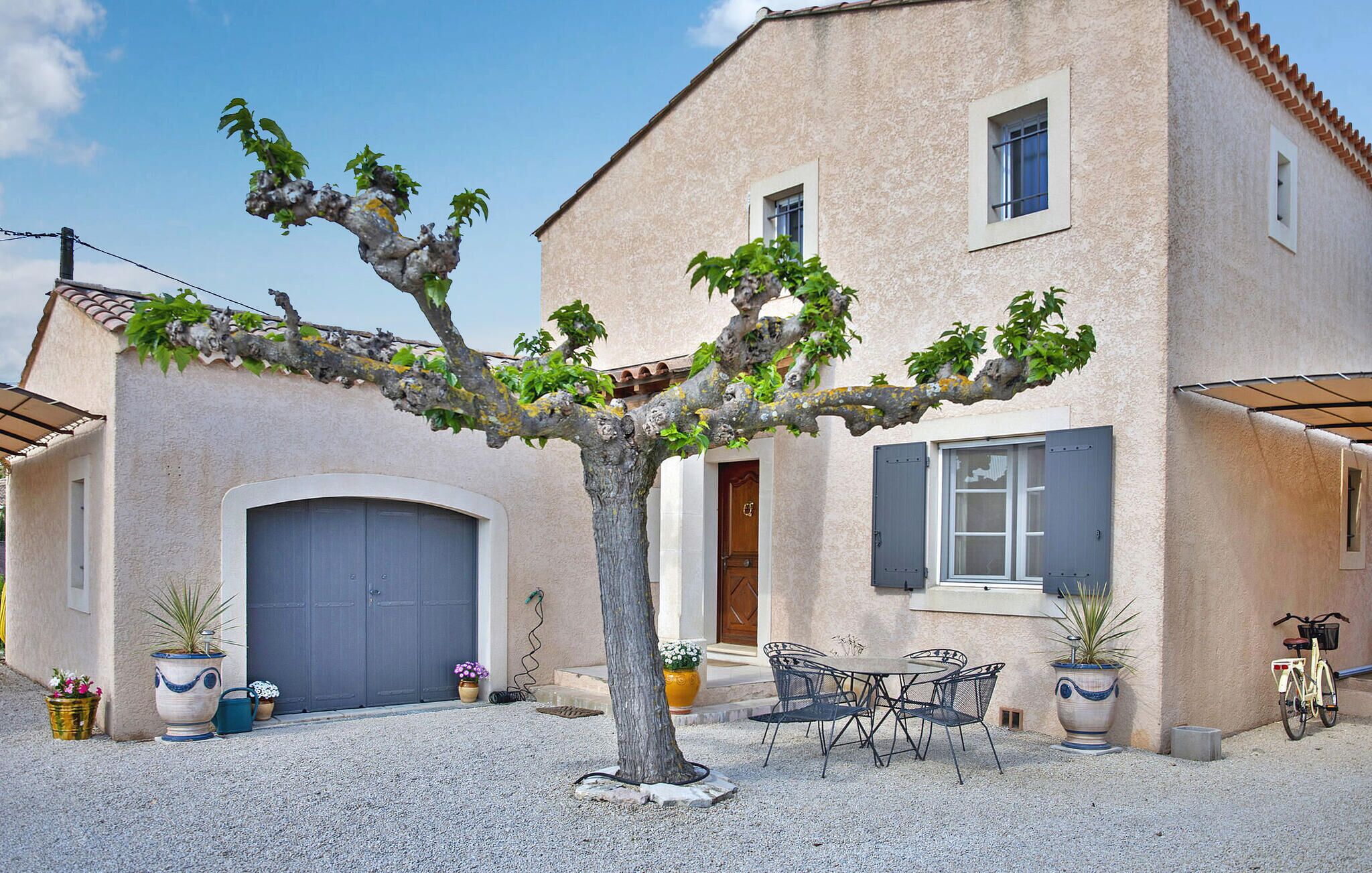 A building with a large garage door, a tree in front, outdoor seating, and a bicycle.