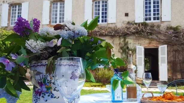 A table set outdoors with a floral vase, wine glasses, and a basket of food.